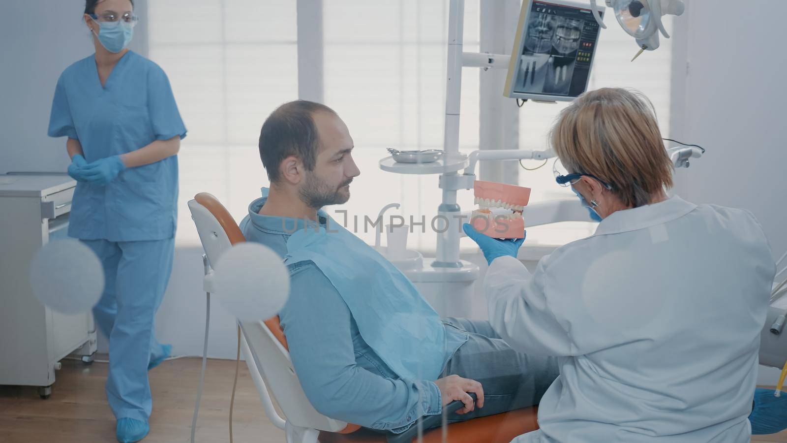 Dentist giving hygiene lesson to patient to clean teeth correctly with toothbrush and toothpaste in stomatology office. Expert showing oral care routine on artificial jaw to prevent caries.