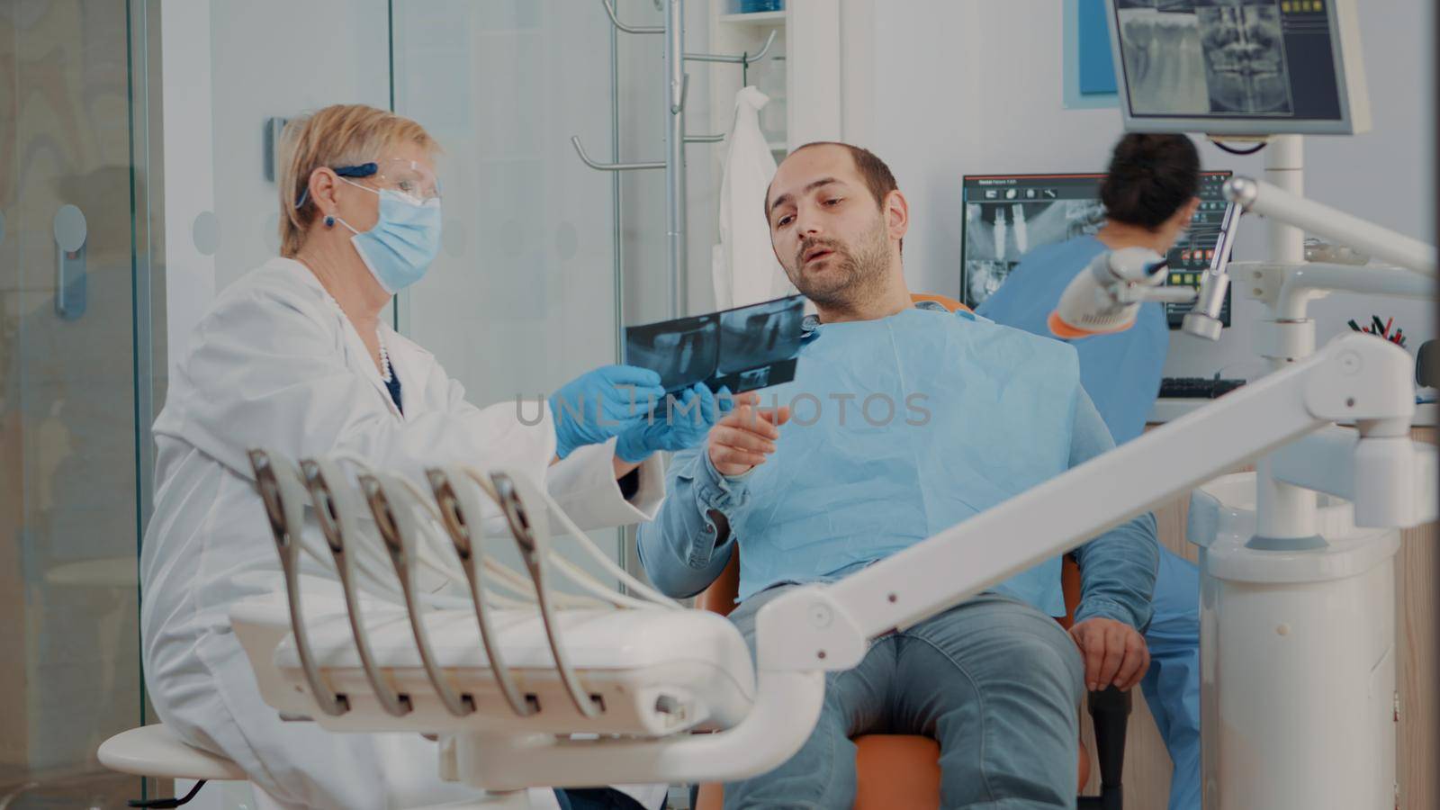 Stomatologist showing x ray scan diagnosis to patient in dentistry cabinet. Dentist holding radiography results to do oral care inspection and cure toothache. Man with caries at appointment.