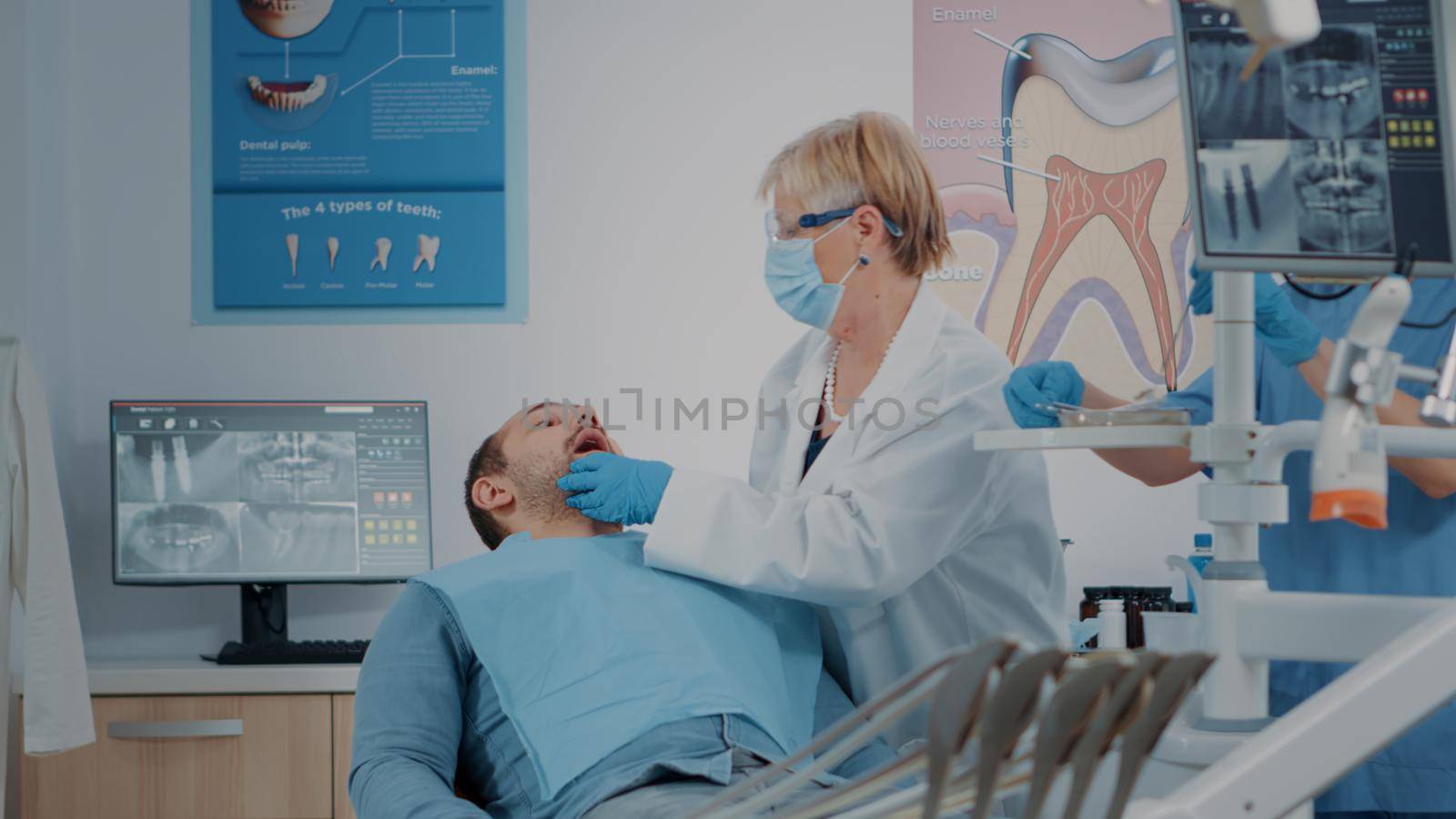 Dentist with face mask using dental tools to examine denture, consulting patient with teeth problems. Stomatology expert doing oral care inspection on man to cure toothache.