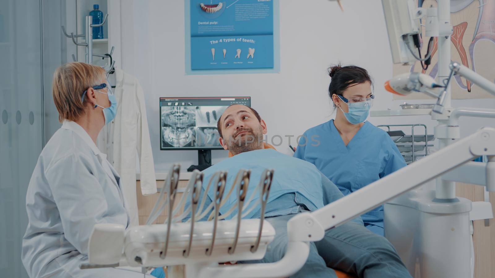 Stomatologist and nurse finishing oral care procedure with patient in dentistry office. Dentist giving mirror to man to look at denture results after surgery and dental examination.