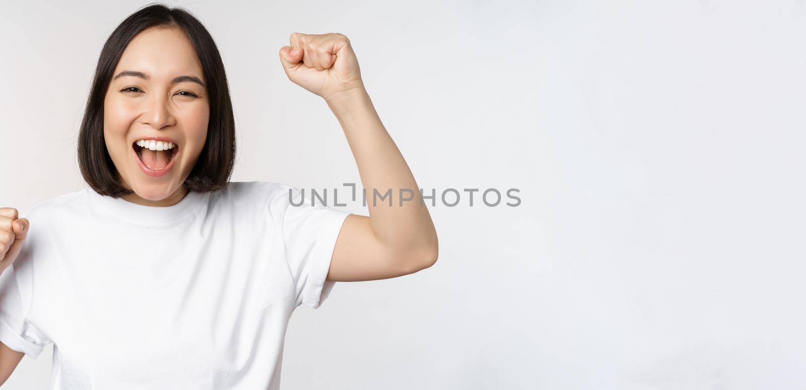 Portrait of enthusiastic asian woman winning, celebrating and triumphing, raising hands up, achieve goal or success, standing over white background by Benzoix