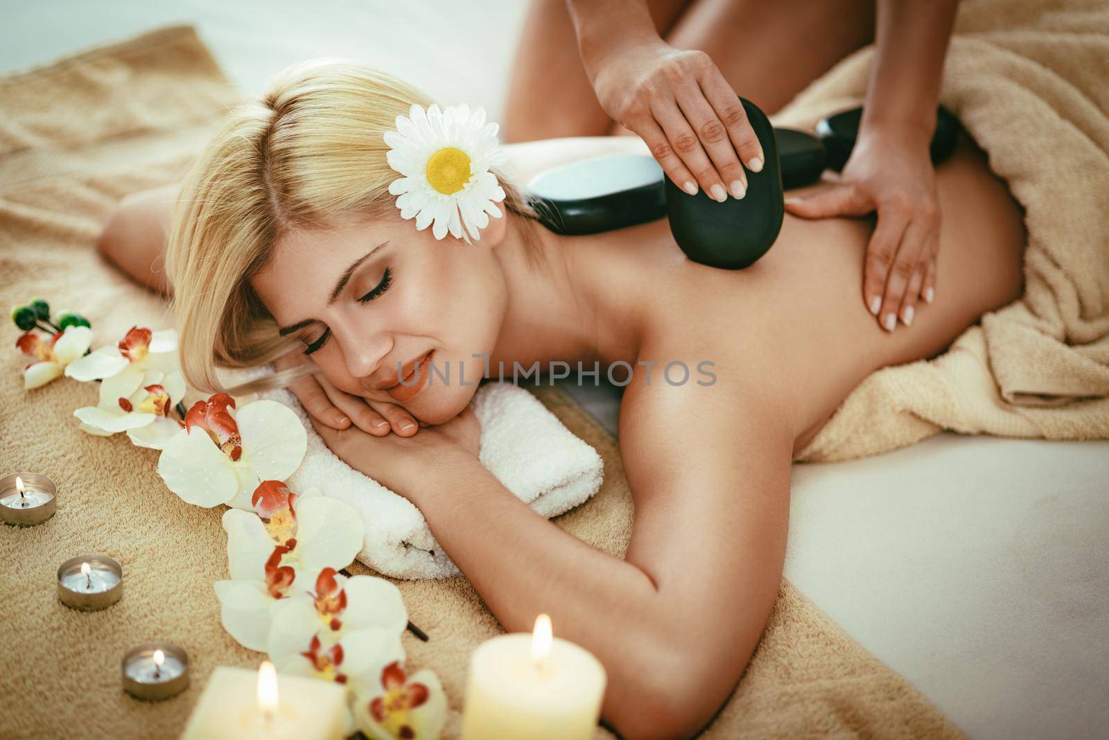 Cute young woman is enjoying during a back massage with warm stones at a spa.