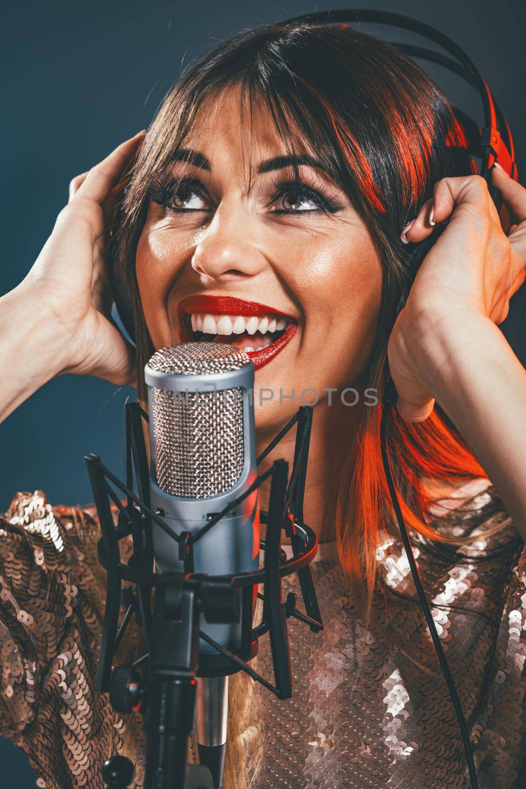 A young woman singer with headphones in front of the microphone. Sing with mouth wide open and with an expression of happiness on her face.