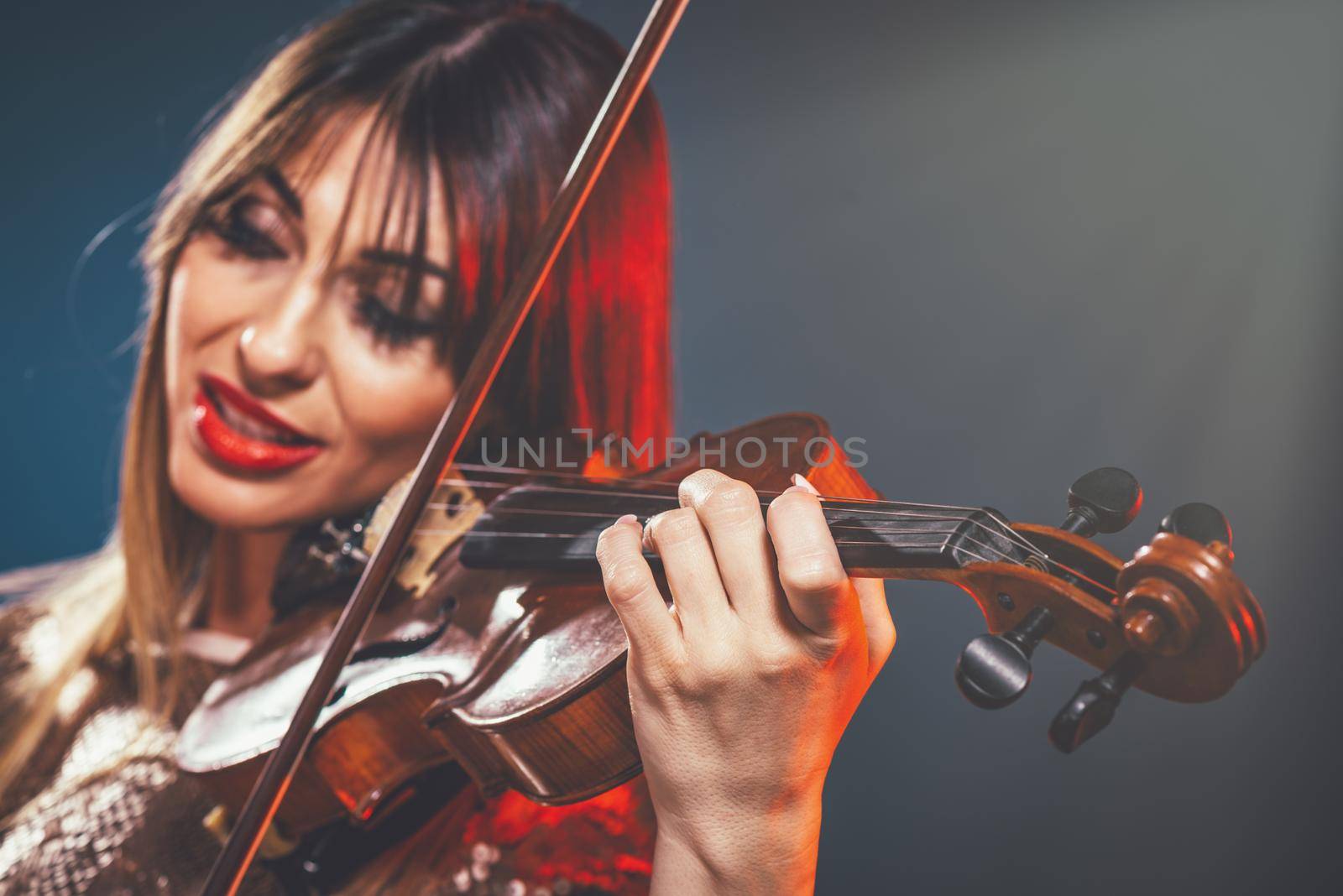 Beautiful young smiling woman in sequin dress playing the classical music on violin.