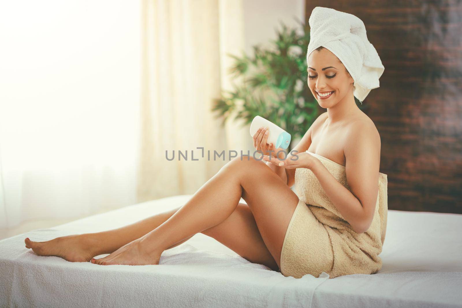 Beautiful young woman applying body lotion during a skin care treatment at a spa. 
