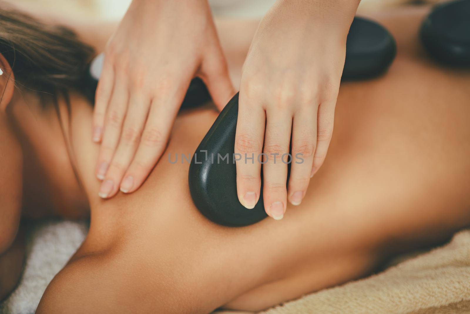 Cute young woman is enjoying during a back massage with warm stones at a spa.