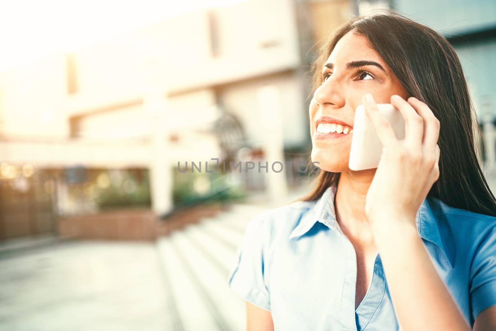 Emotional portrait of a happy and beautiful young businesswoman talking on a smartphone on the background of a business center.