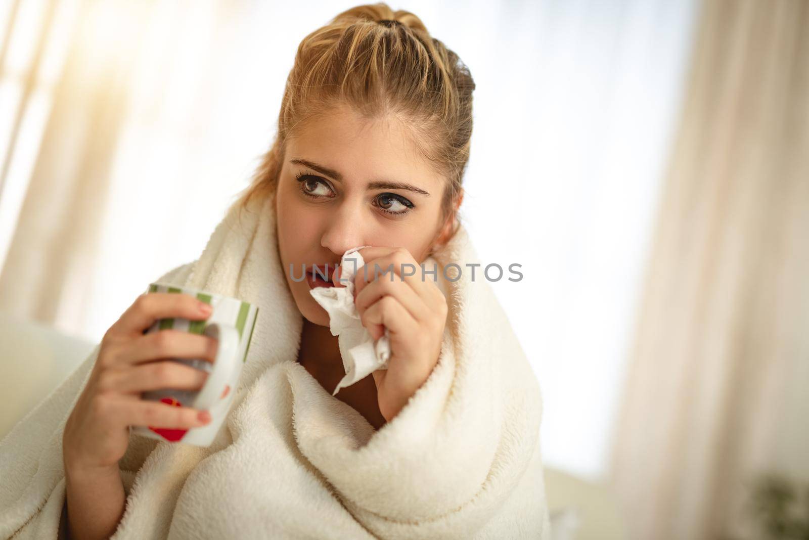 A beautiful girl with handkerchief to her nose and holding a cup of tea.