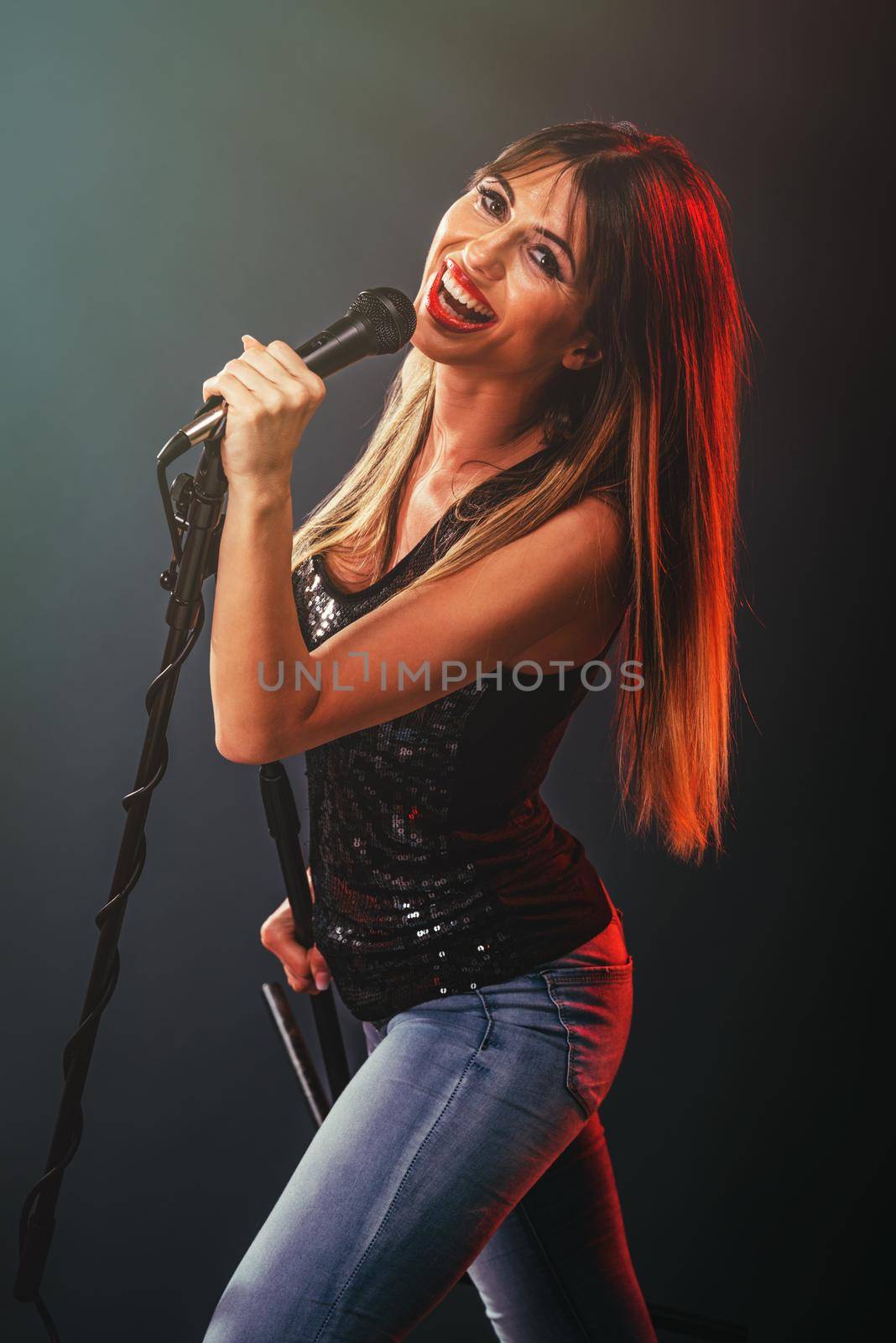 A young woman singer in front of the microphone. Sing with mouth wide open and with an expression of happiness on her face.