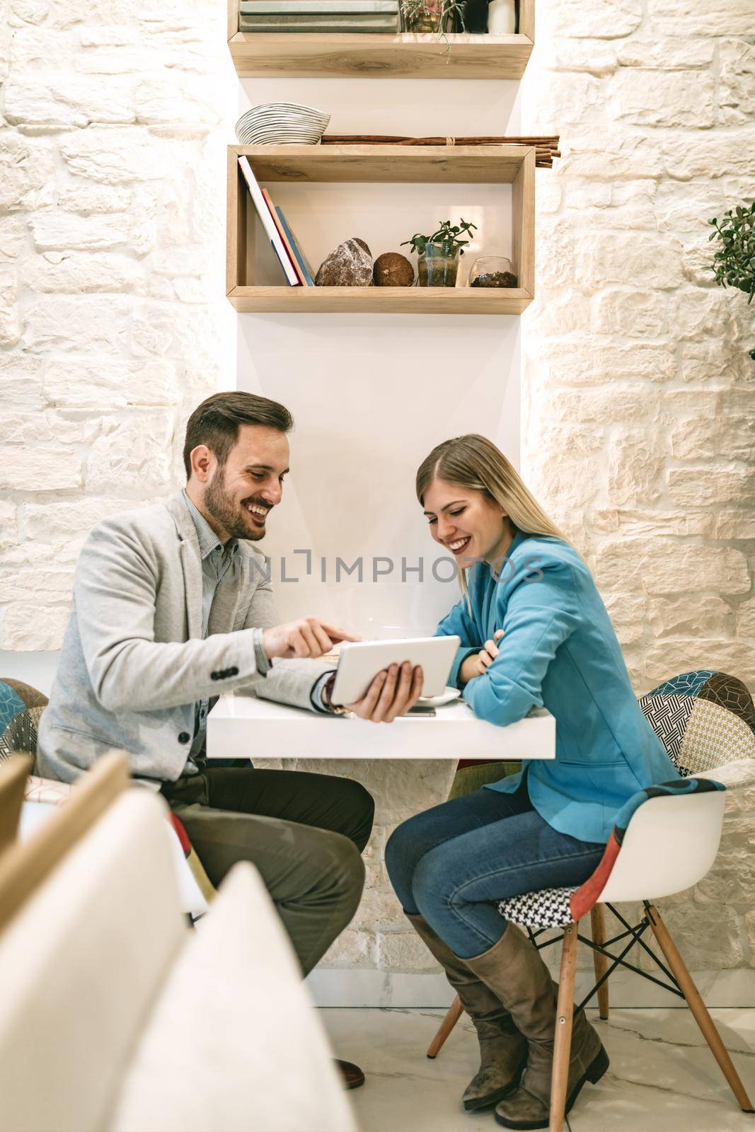 Two beautiful young smiling people sitting at cafe and working on digital tablet.