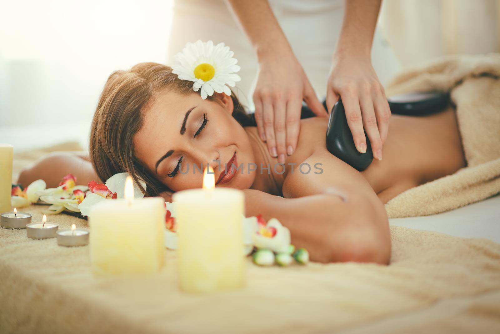 Cute young woman is enjoying during a back massage with warm stones at a spa.