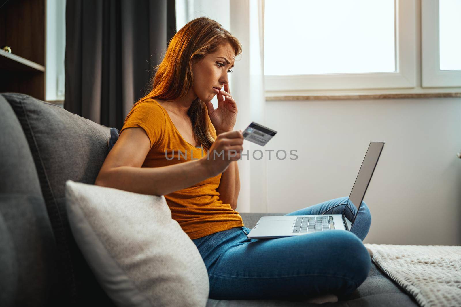 Shot of a worried young woman doing online shopping on her laptop while sitting on the sofa at home.