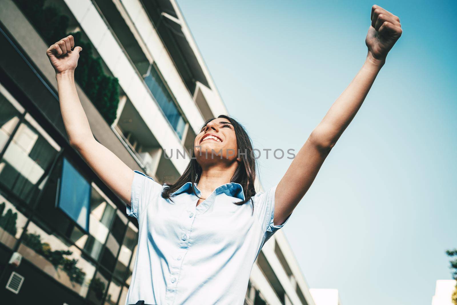 Emotional portrait of a happy and beautiful young businesswoman celebrating success arms raised on the background of a business center.