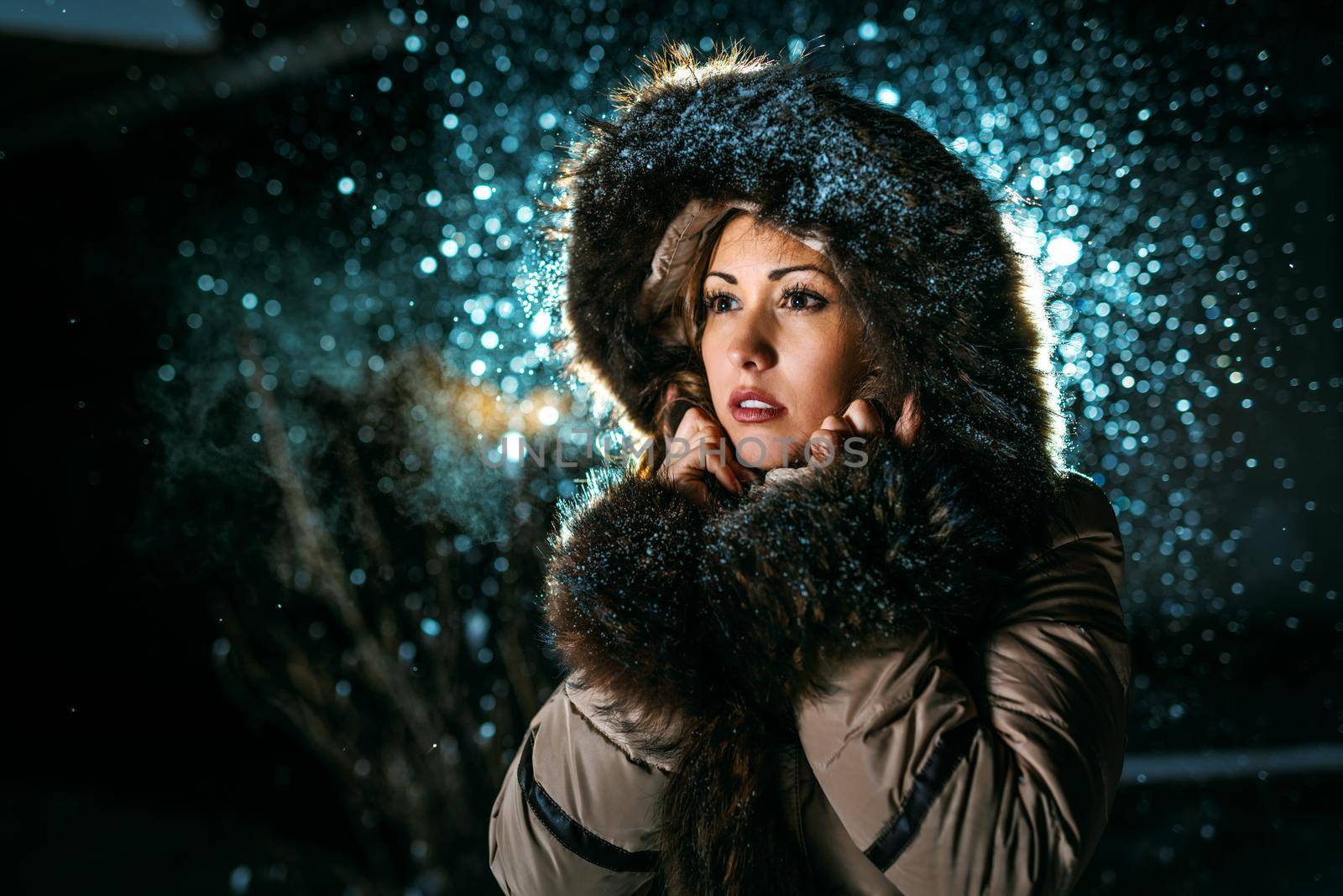 Beautiful young scared woman in winter jacket with fur hood worries and is looking away waiting for somebody.