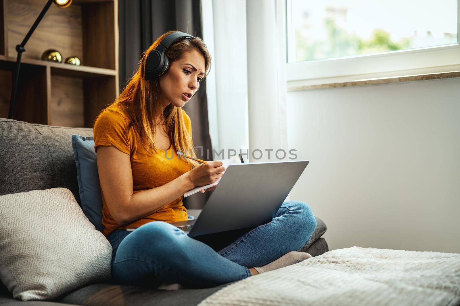 Shot of a young female student using a laptop and headphones and learning at home.