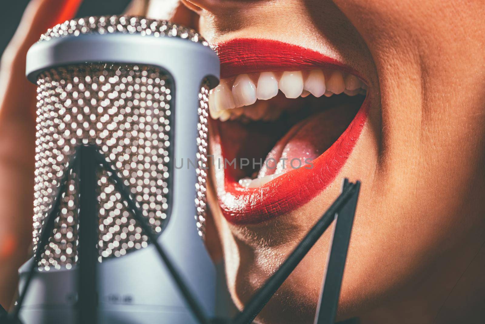 Close-up of a female open mouth with red lipstick singing on the microphone.
