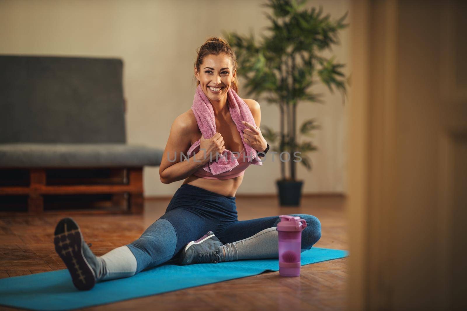 Young smiling woman is doing stretching exercises in the living room on floor mat at home in morning sunshine.