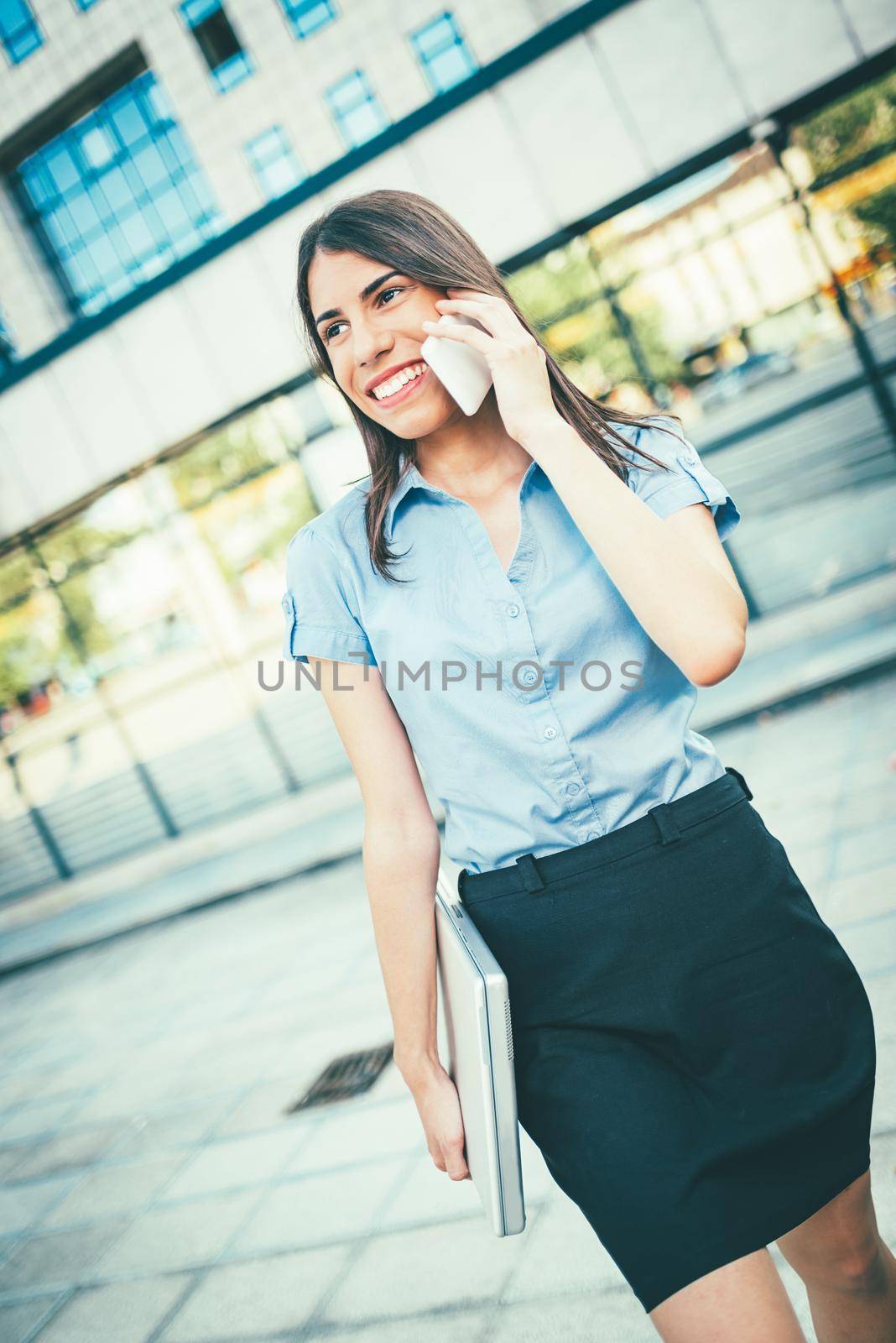Emotional portrait of a happy and beautiful young businesswoman talking on a smartphone and reading information in a file document on the background of a business center.