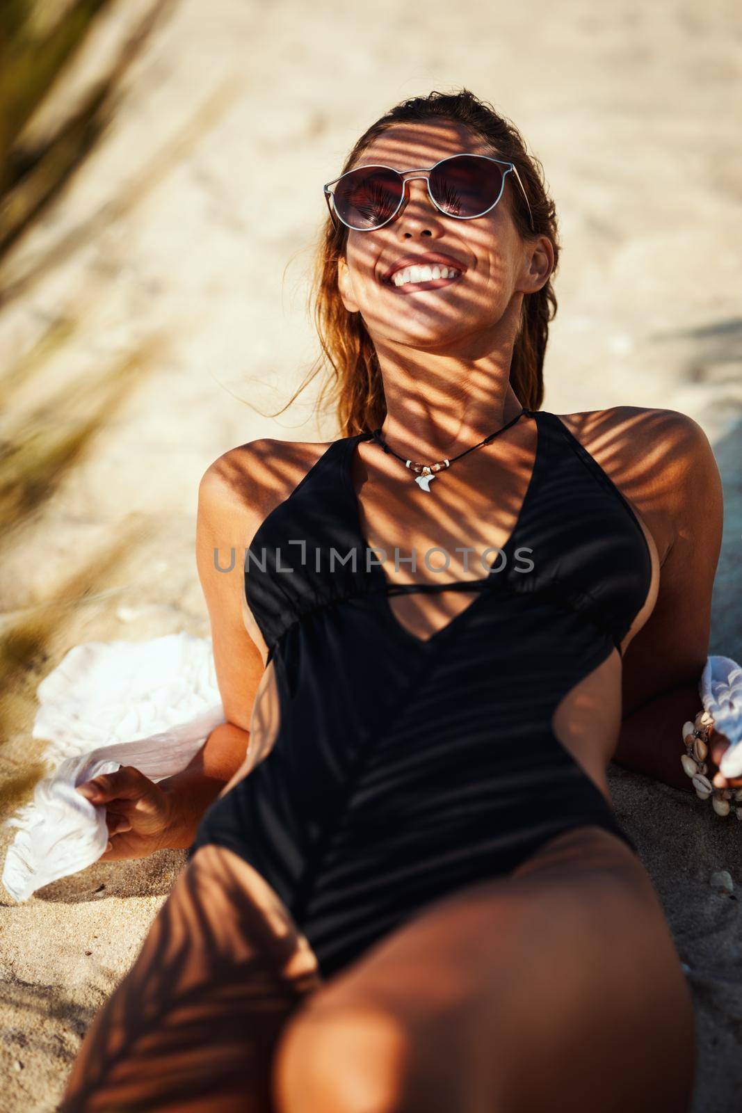 Shot of an attractive young woman is sunbathing and enjoying under the shade of a palm tree at the beach.