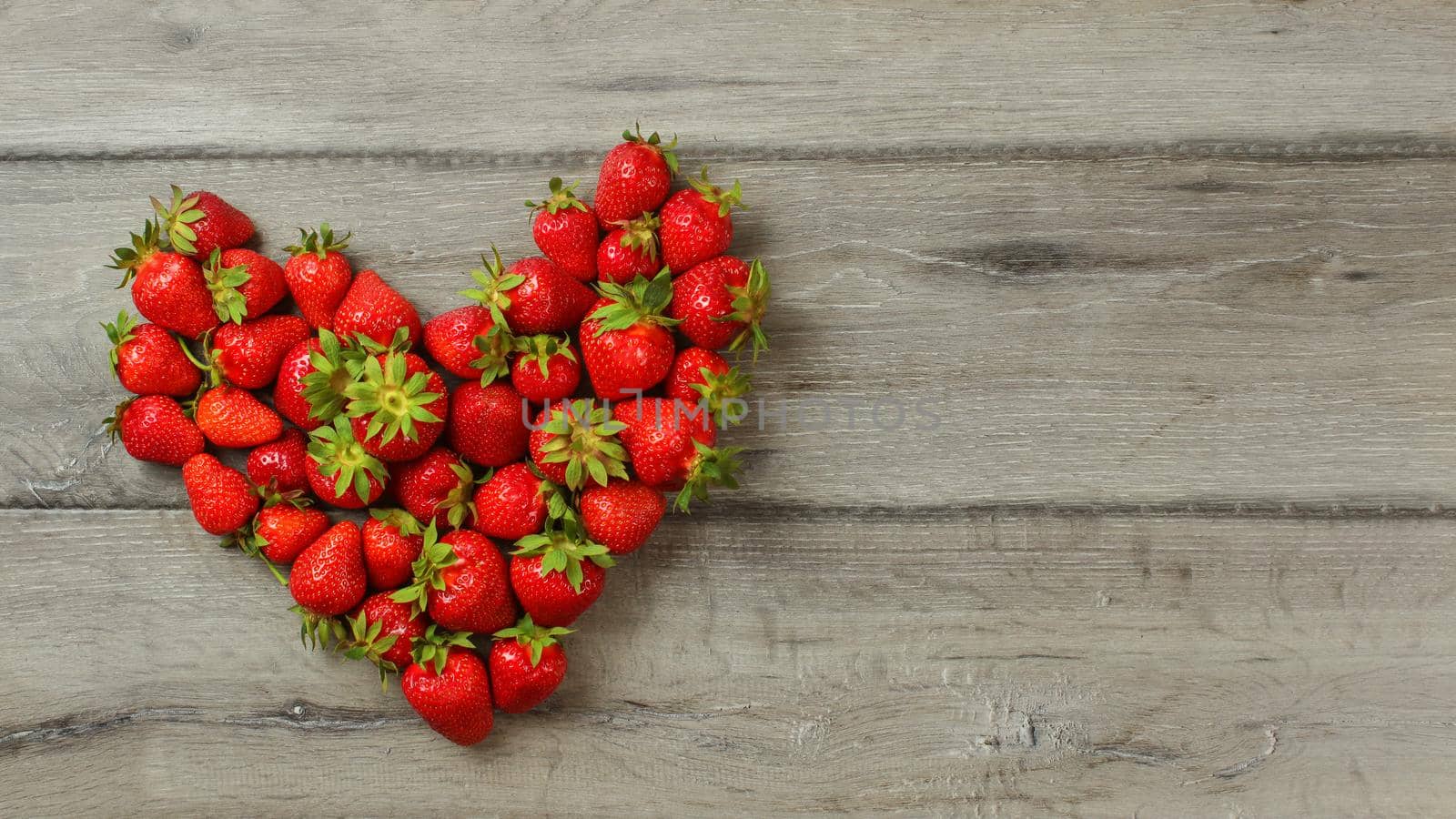 Tabletop view, strawberries on wood desk, arranged in shape of heart, space for text right.