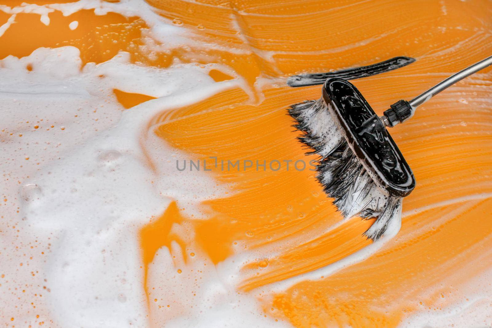 Brush leaving strokes in white foam and soap on yellow car washed in carwash.