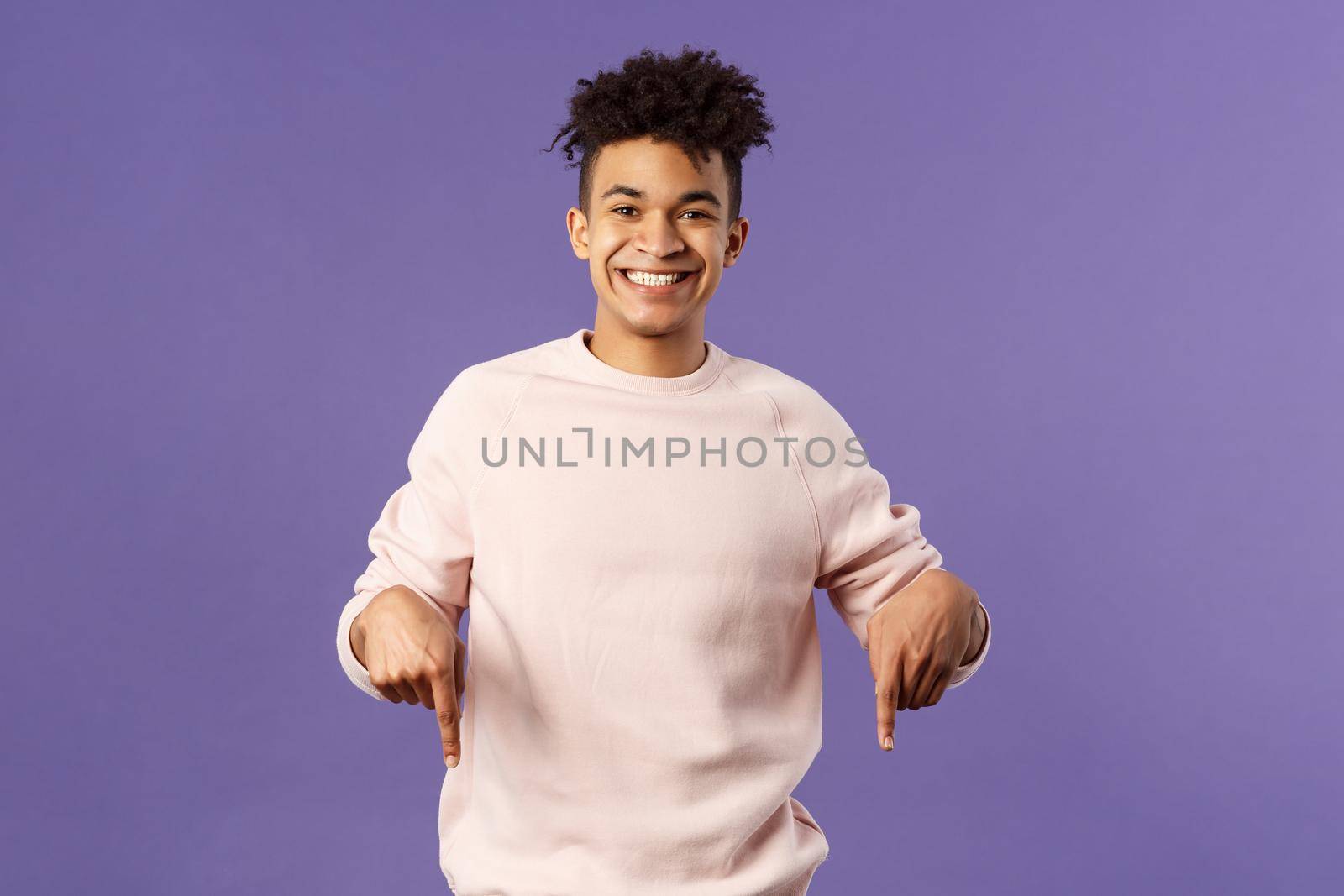 Portrait of cheerful, happy young 25s man recommending product, showing promo of product, delivery service, online shop or appllication, pointing fingers down, smiling pleased camera.
