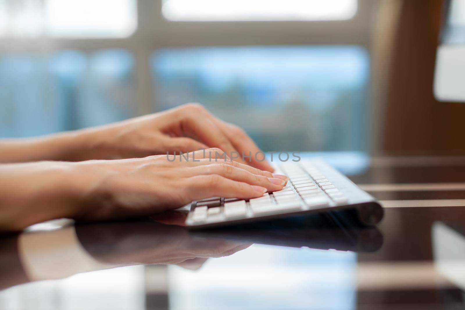 Female hands typing text on the keyboard while exchanging messages with friends via social networks using a computer laptop. A female office worker checks her email while sitting at a desk.