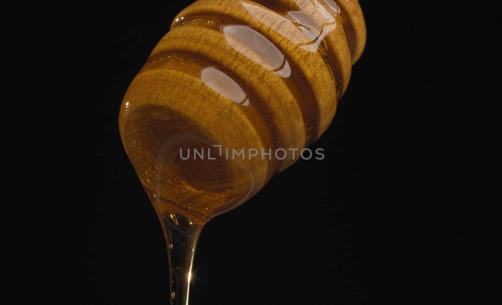 Extreme close up fresh honey pouring from honey spoon on black background. Healthy fresh food concept. Macro