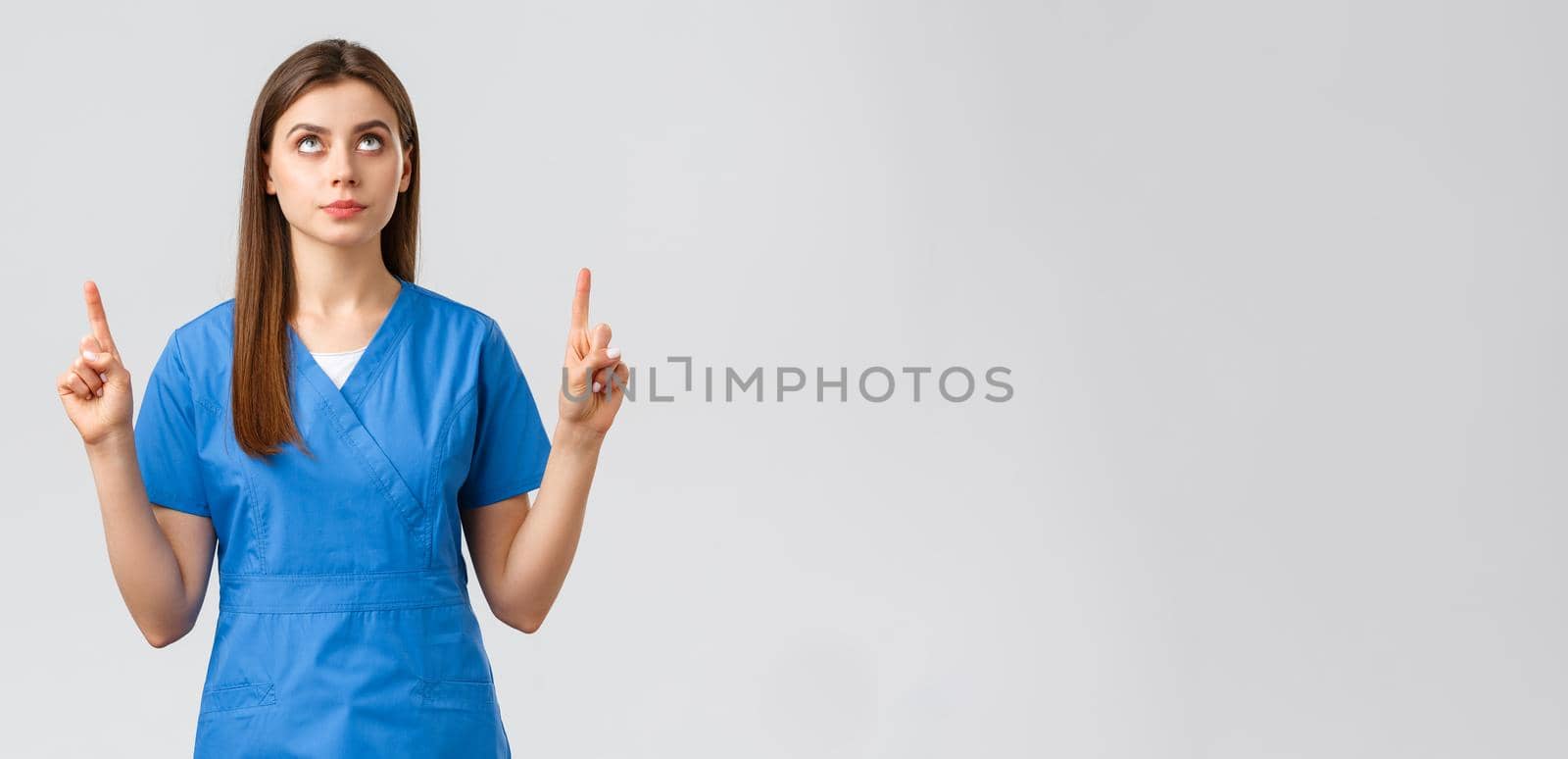 Healthcare workers, prevent virus, covid-19 test screening, medicine concept. Concerned, serious and focused female doctor or nurse in blue scrubs, pointing fingers and looking up at banner.
