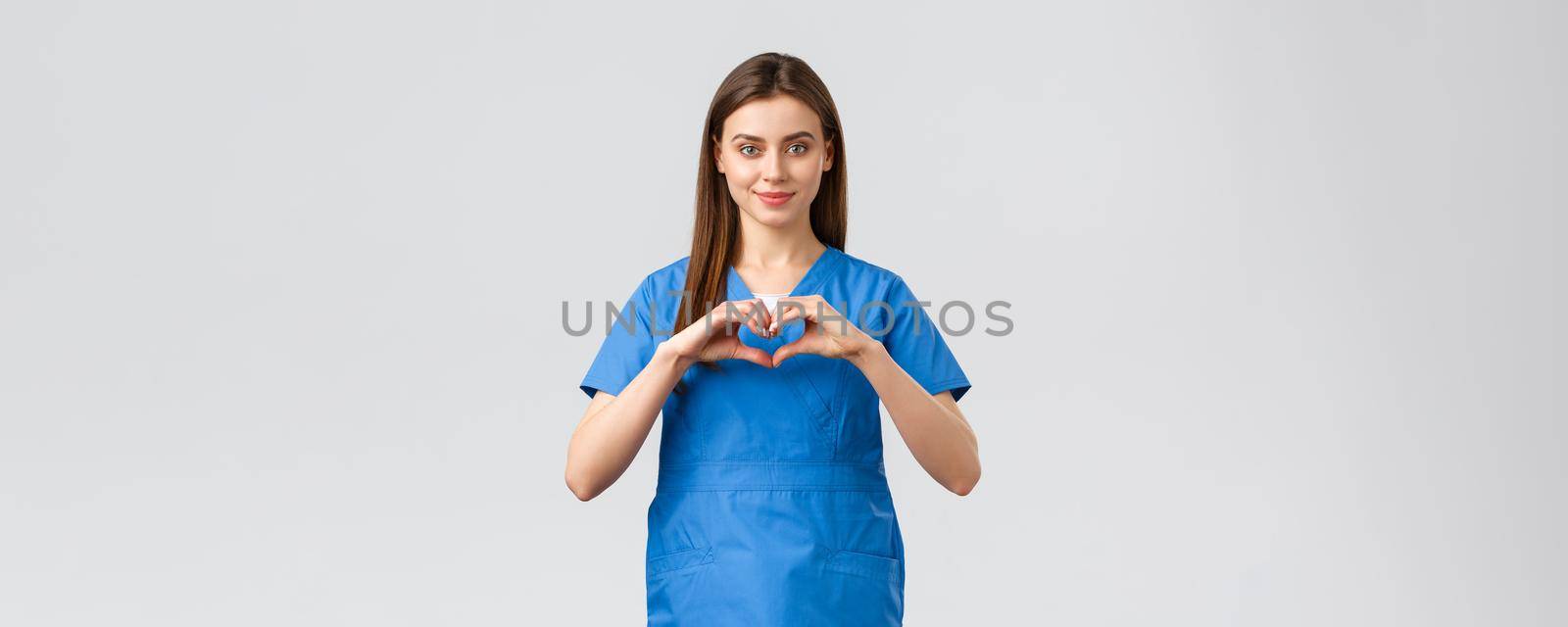 Healthcare workers, prevent virus, insurance and medicine concept. Smiling attractive female doctor, nurse in blue scrubs stay safe home, show heart sign, express respect to coronavirus fighters by Benzoix