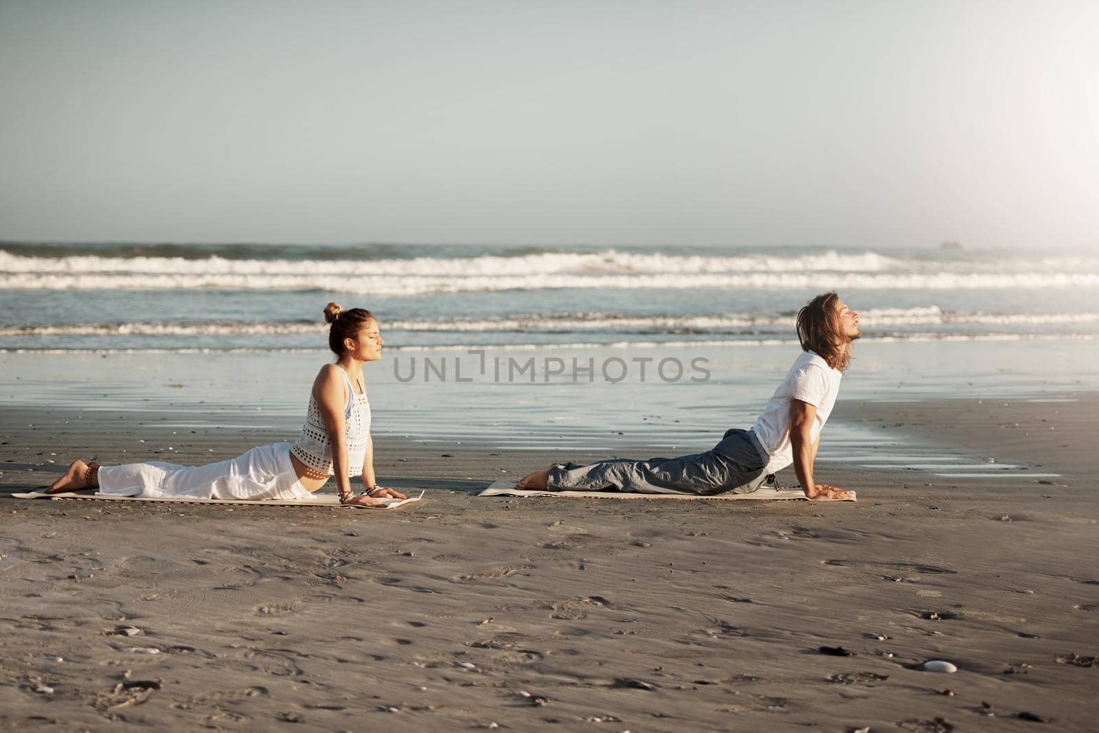 Shot of a young couple practising yoga together on the beach.