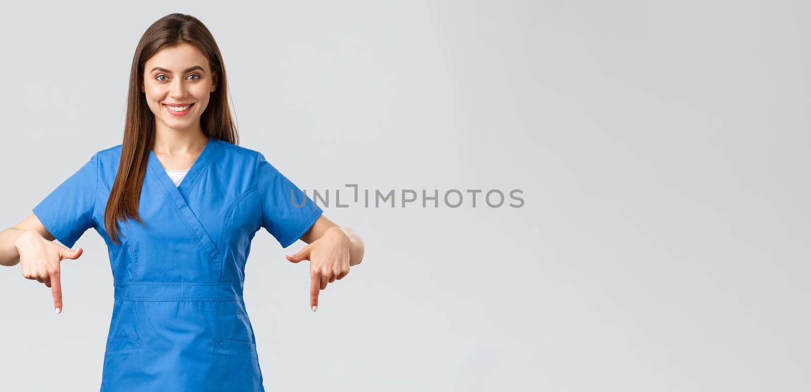 Healthcare workers, prevent virus, covid-19 test screening, medicine concept. Smiling confident nurse, doctor or intern in blue scrubs, pointing fingers down as give patients information by Benzoix