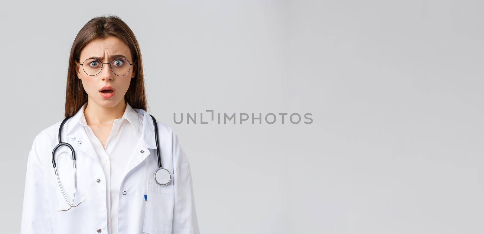 Healthcare workers, medicine, insurance and covid-19 pandemic concept. Shocked nervous female doctor in white scrubs and glasses, doctor gasping and staring concerned camera by Benzoix