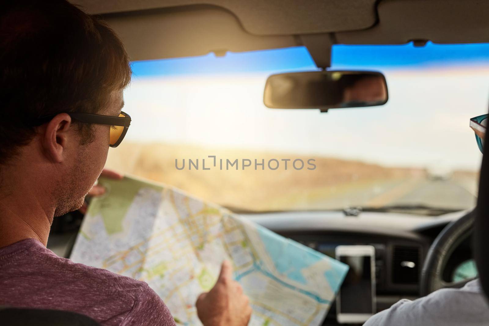 We should reach this destination in twenty minutes. Shot of two young friends reading a map while driving in their vehicle and heading to their destination. by YuriArcurs