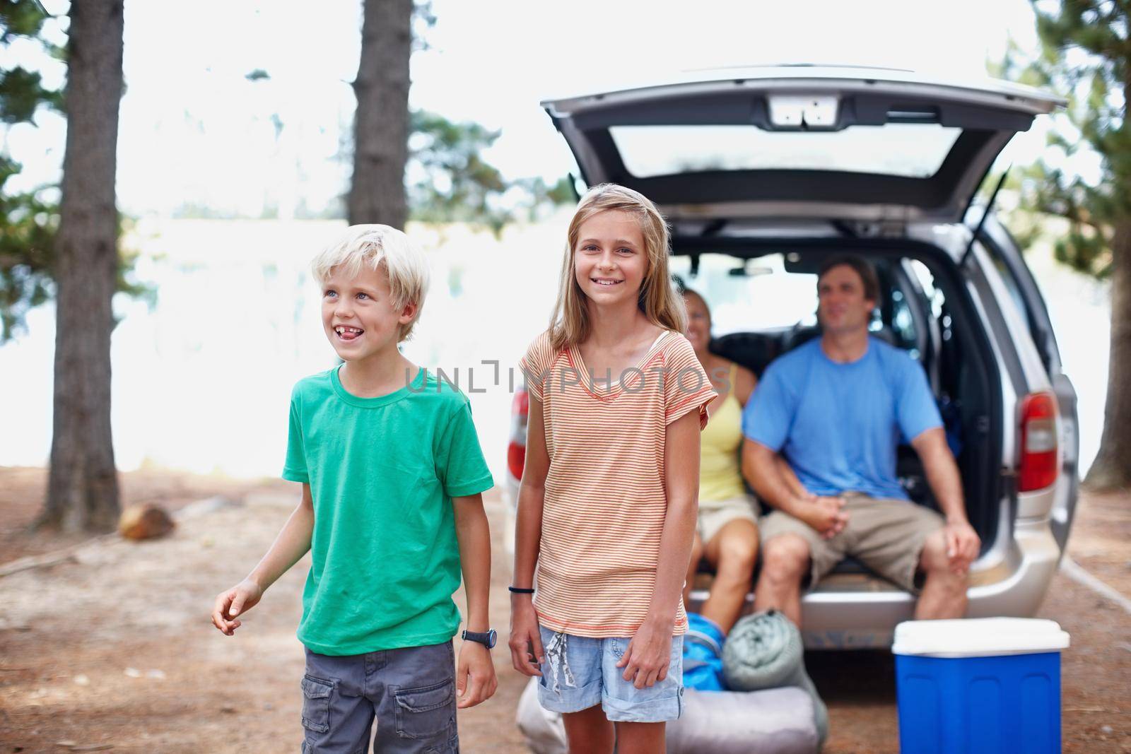 Young siblings enjoying vacation. Portrait of brother and sister enjoying their holiday with parents sitting in the car. by YuriArcurs