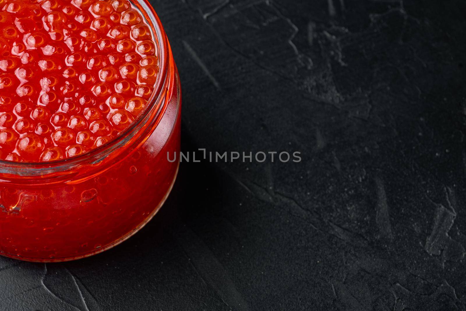 Red salmon caviar jar, on black background with copy space for text