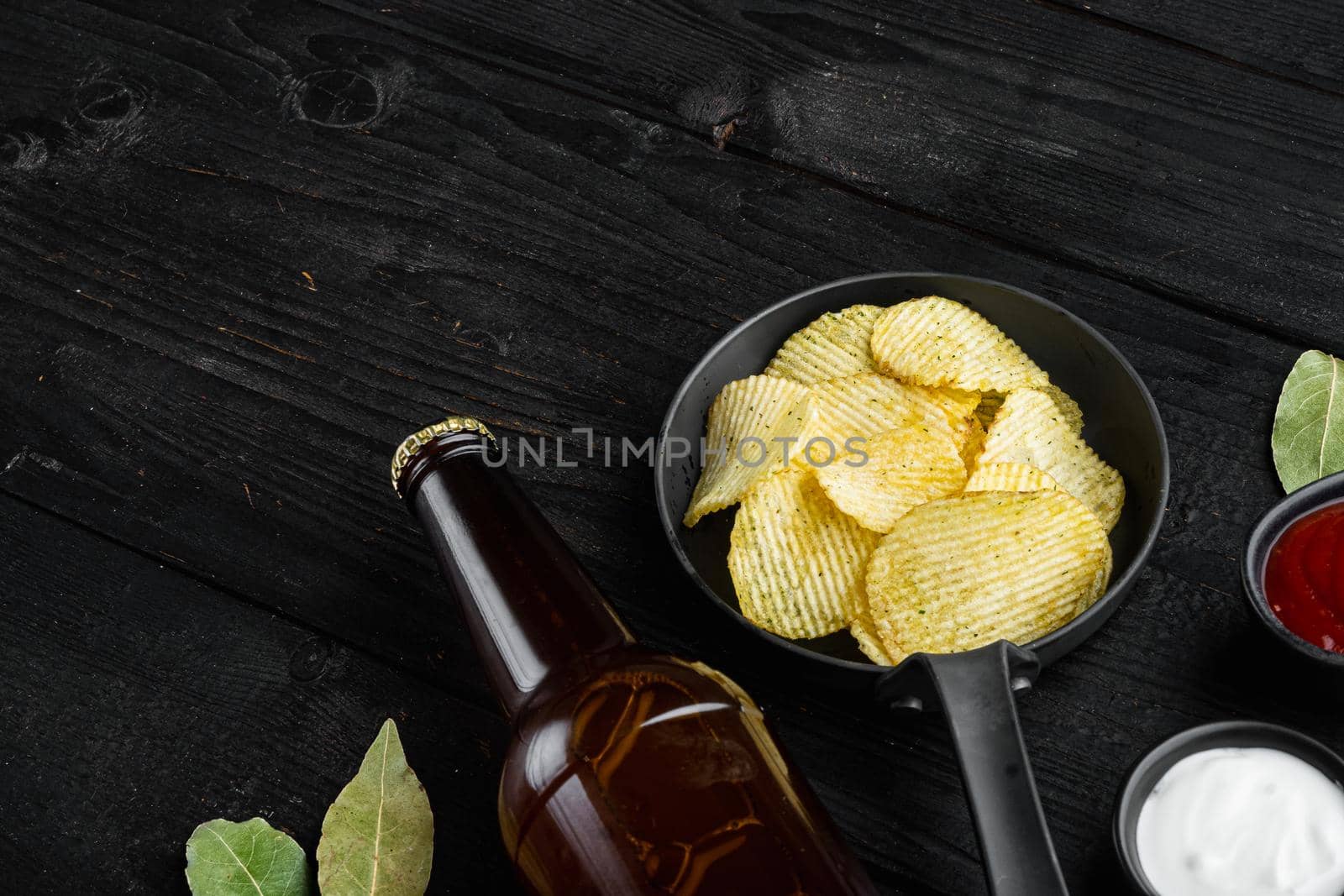 Home made potato chips set, and bottle of beer, on black wooden background, with copy space for text