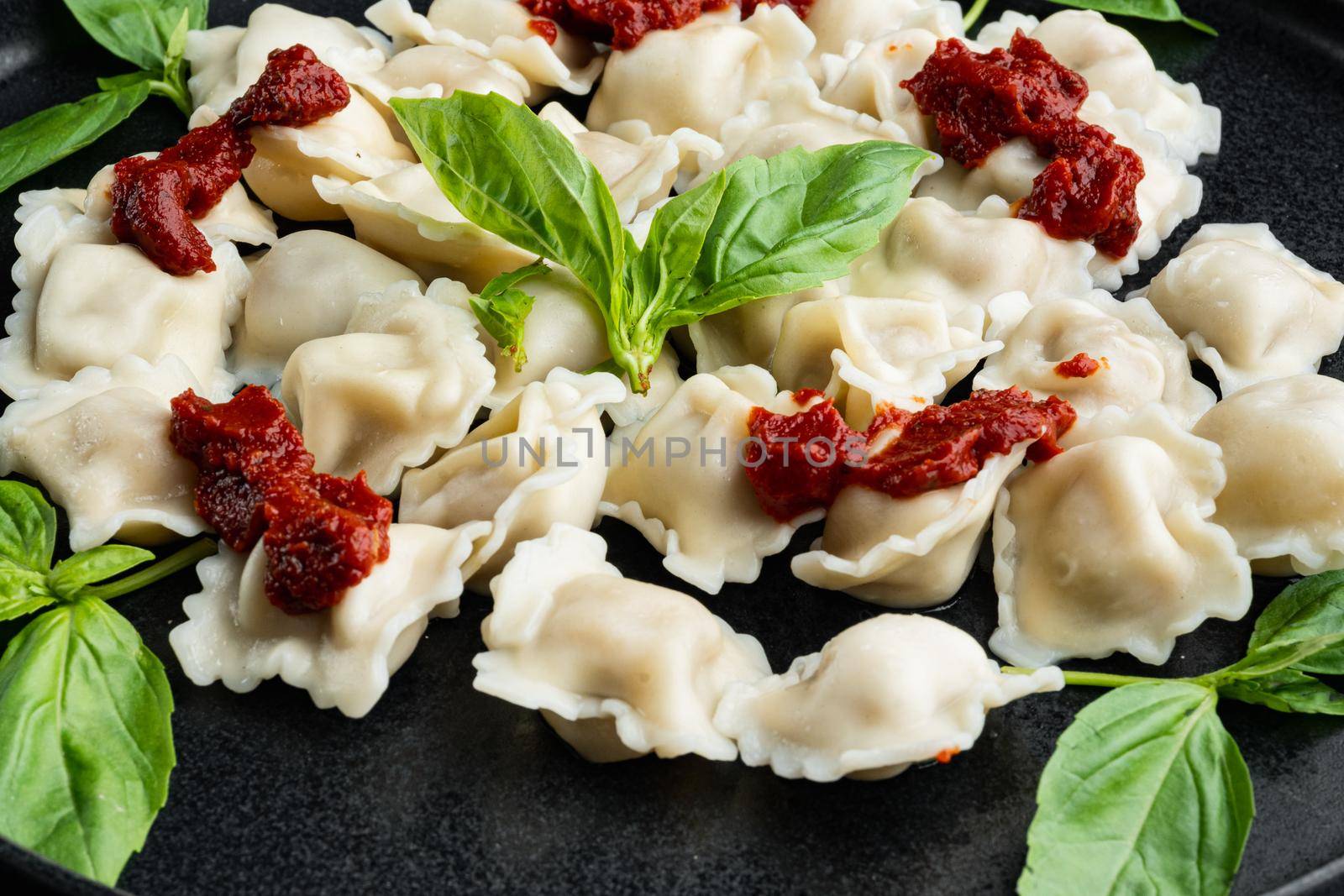 Ravioli pasta with mushroom cream sauce and cheese - Italian food style set with basil parmesan and tomatoe on black plate, on black background