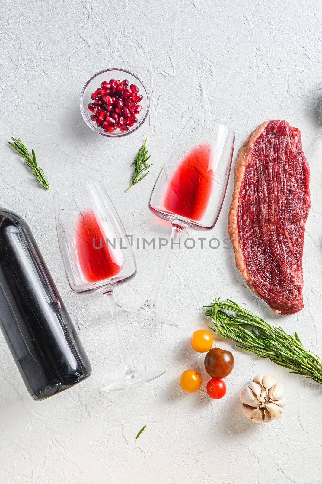 Two glasses of red wine near bottle and beef steaks over white concrete background, top view. by Ilianesolenyi