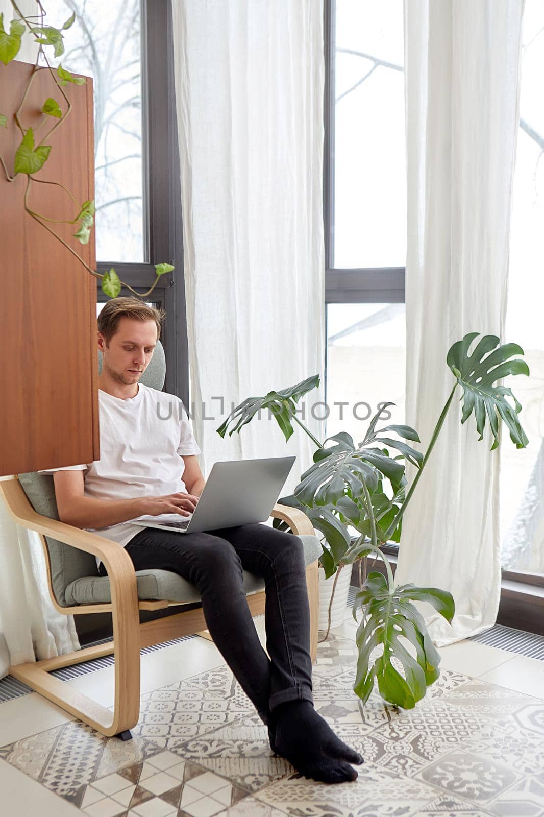 Man working using laptop at home while sitting in chair by Demkat