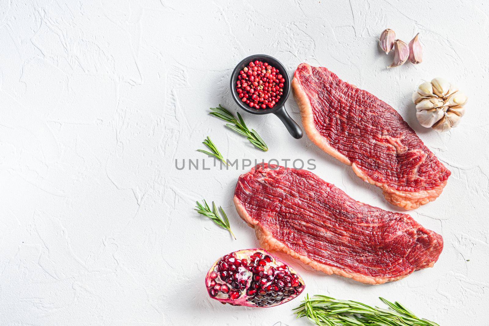 Two picanha beef steaks with rosemary and garnet, over white background, top view with space for text
