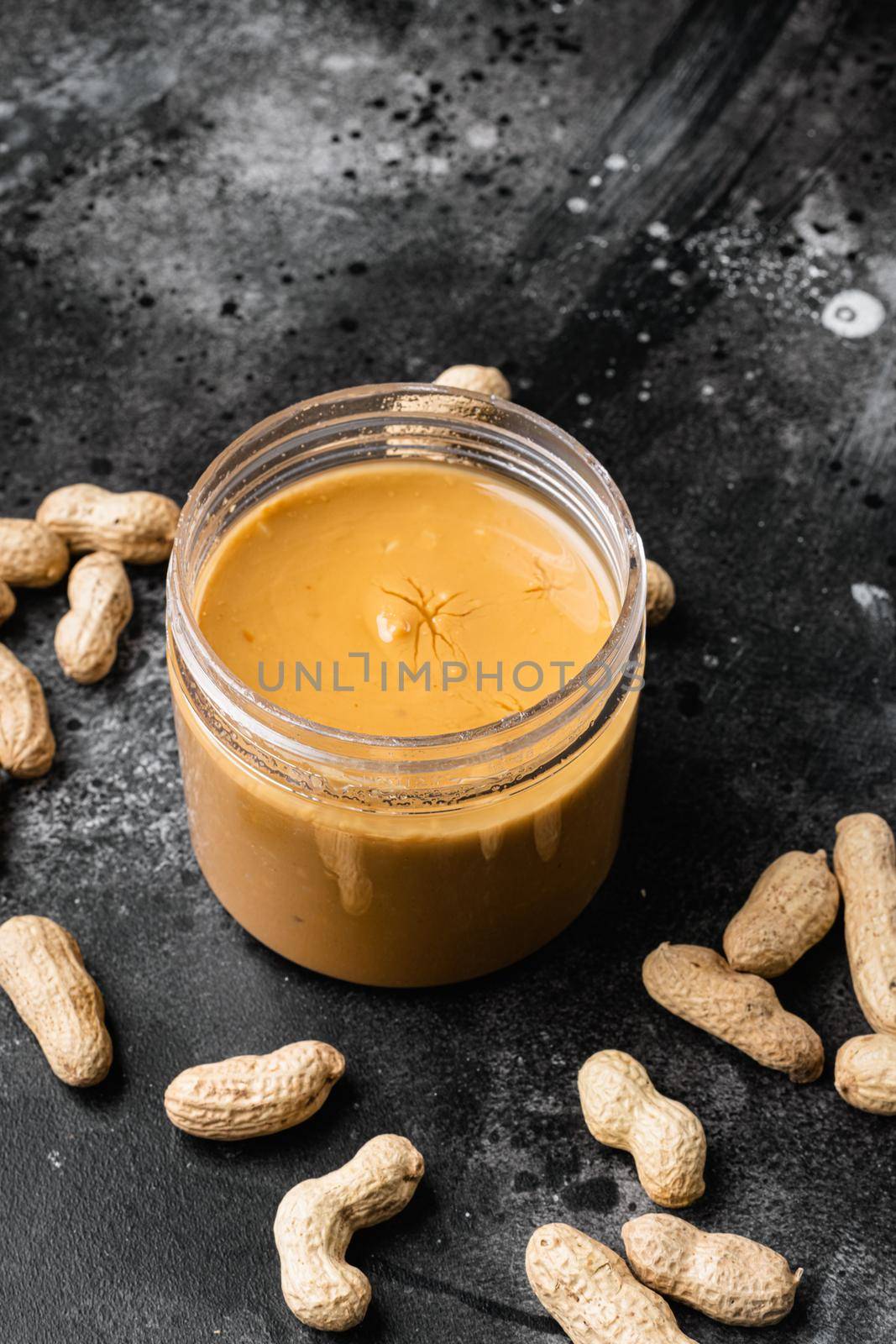 Jar with peanut butter with peanuts set, on black dark stone table background, with copy space for text