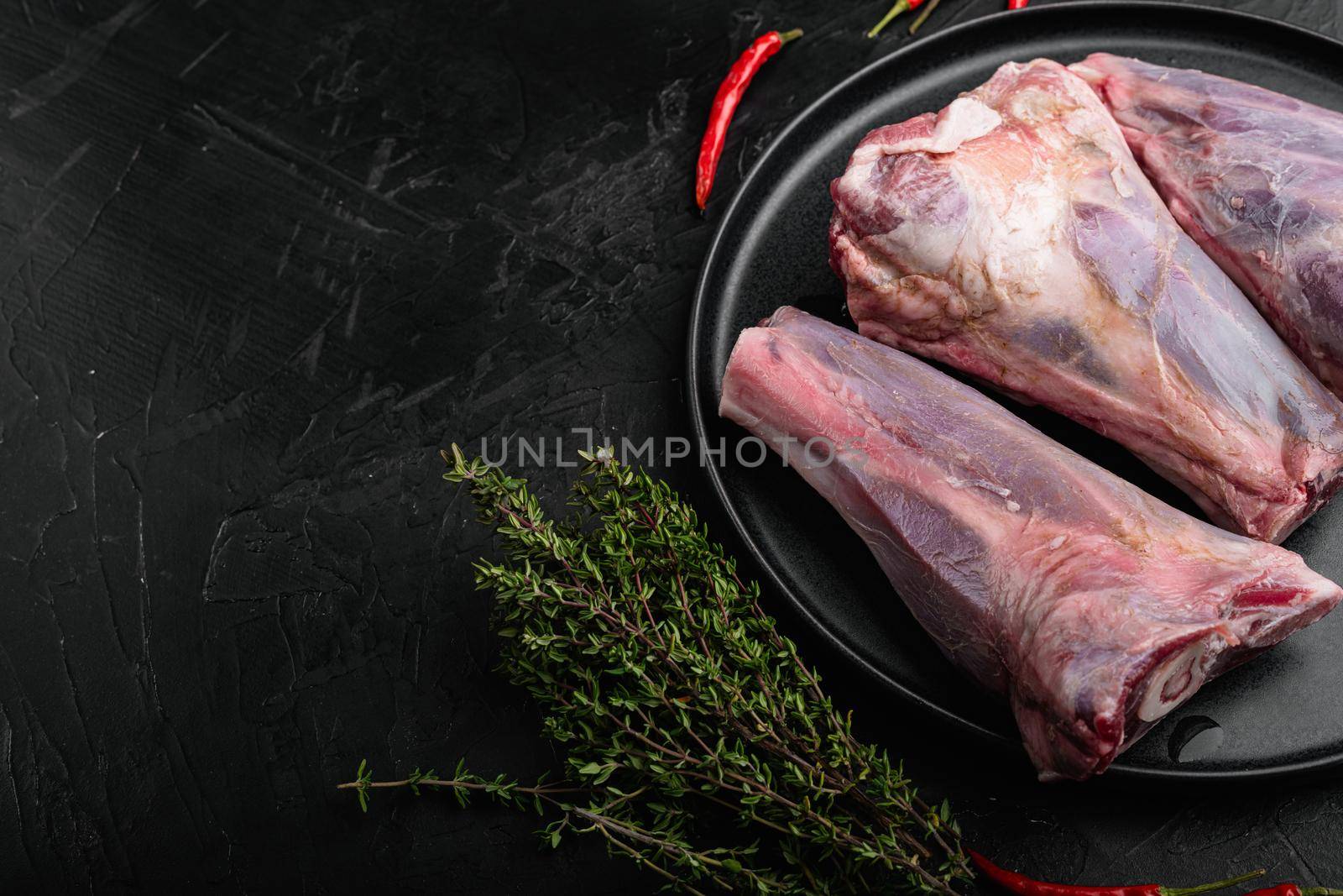 Raw lamb shanks with ingredients set, on black dark stone table background, with copy space for text