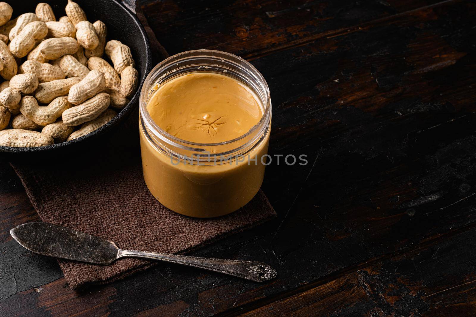 Jar with peanut butter with peanuts set, on old dark wooden table background, with copy space for text