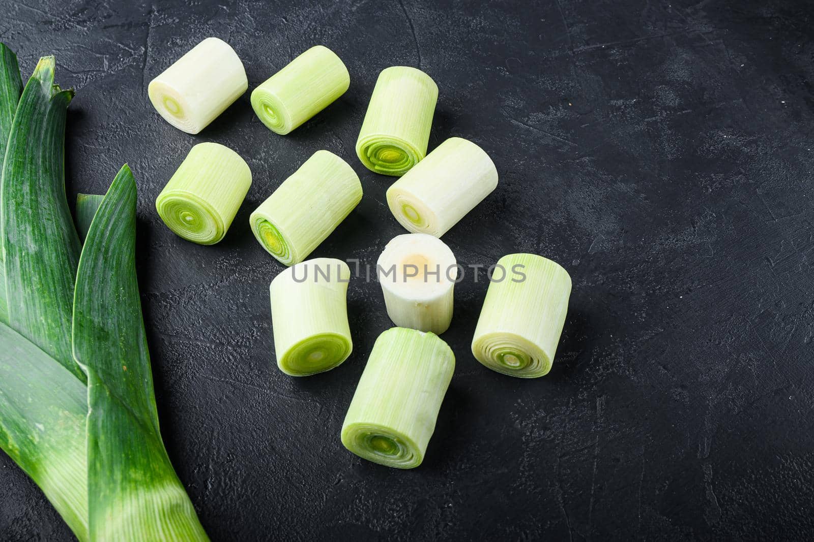 Green leeks sultan oninon uncooked with herbs ingredients , on textured black background top view with space for text