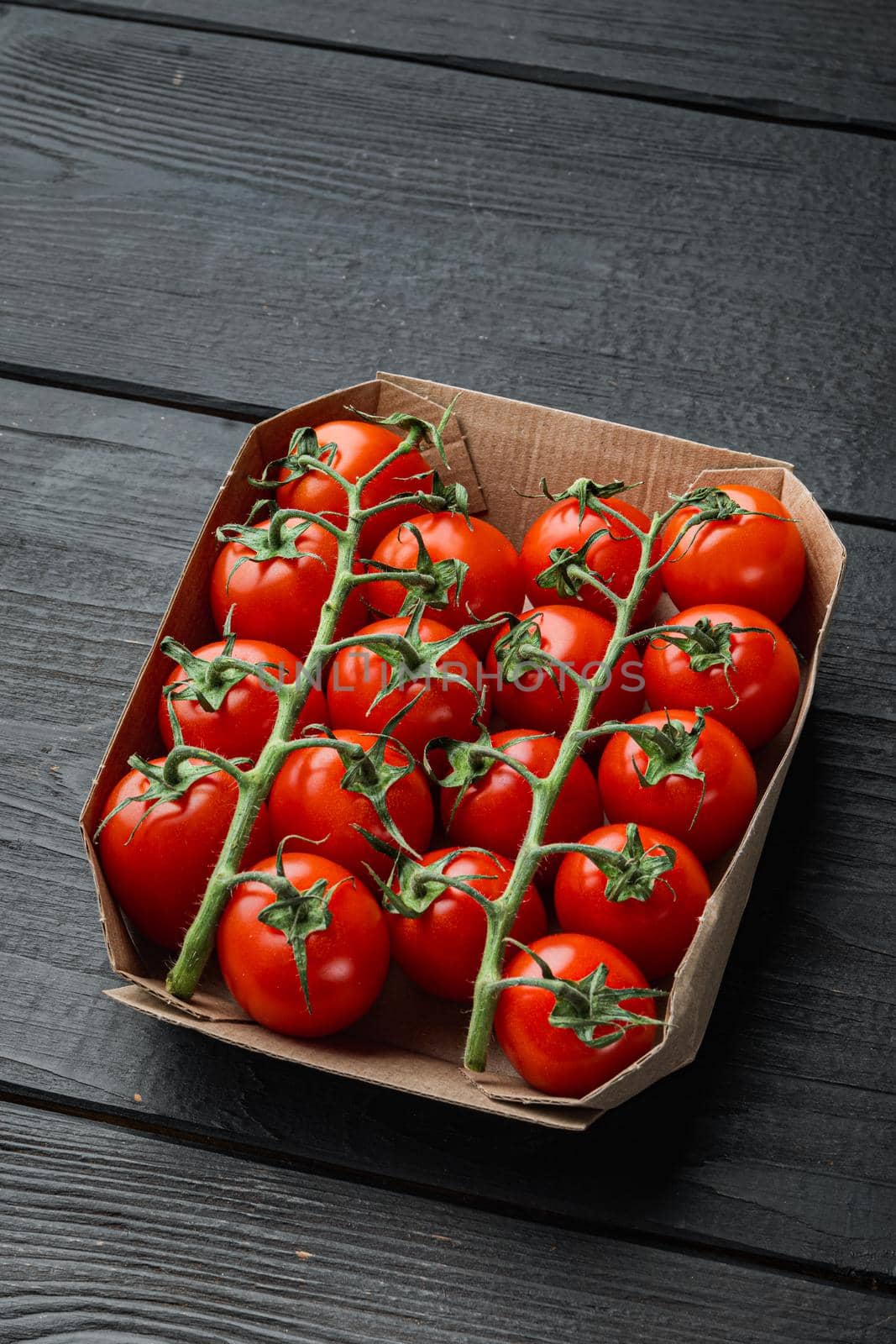 Ripe cherry tomatoe in tray, on black wooden table by Ilianesolenyi