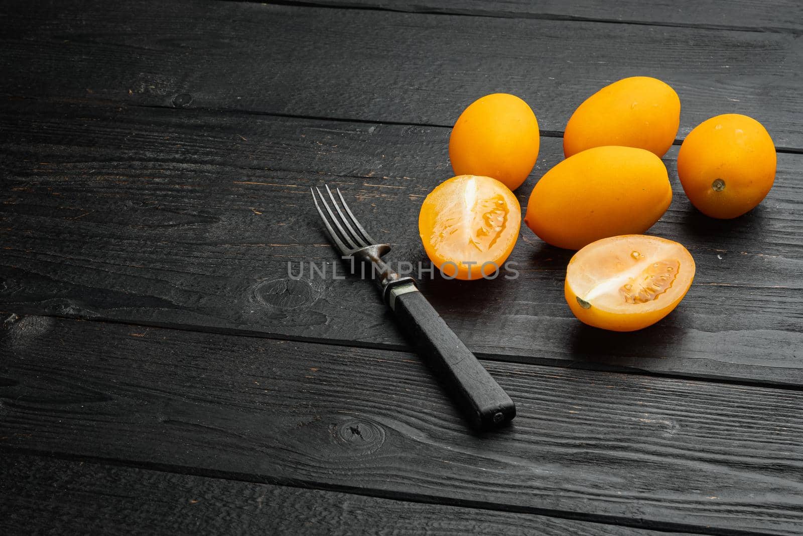Ripe Yellow plum tomatoes set, on black wooden table background, with copy space for text