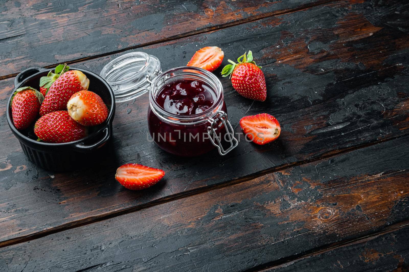 Jars of strawberry jam with berries, on old dark wooden table background with copy space for text