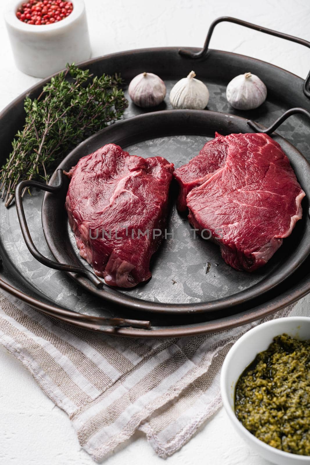 Raw seasoned rump steaks beef meat, on white stone table background by Ilianesolenyi
