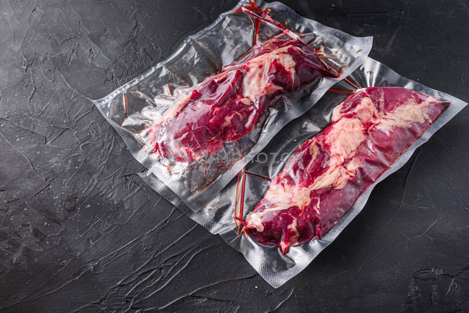 Chuck Tenders beef steak in vacuum sealed bag on black textured background side view space for text. by Ilianesolenyi